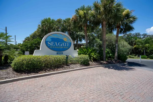 a sign board with flower plants and large trees