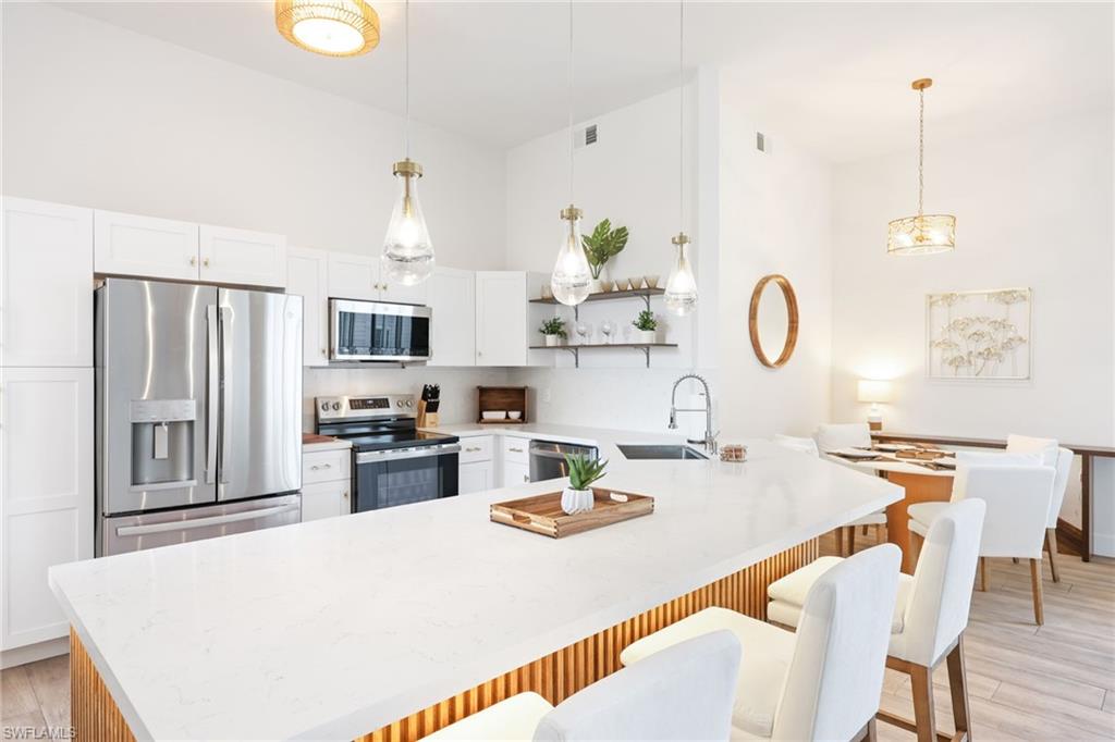 2711 Citrus Lake Drive, Unit F305 Naples, FL 34109 - Photo 18 of 50 a kitchen with stainless steel appliances granite countertop a stove a refrigerator a kitchen island a dining table and chairs with wooden floor