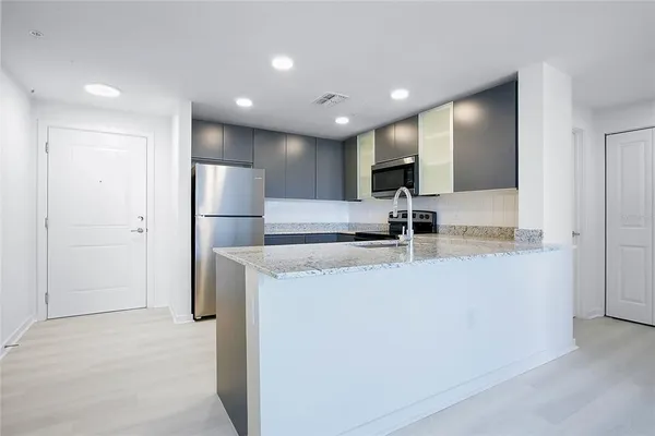 a view of kitchen with stainless steel appliances granite countertop refrigerator sink and white cabinets