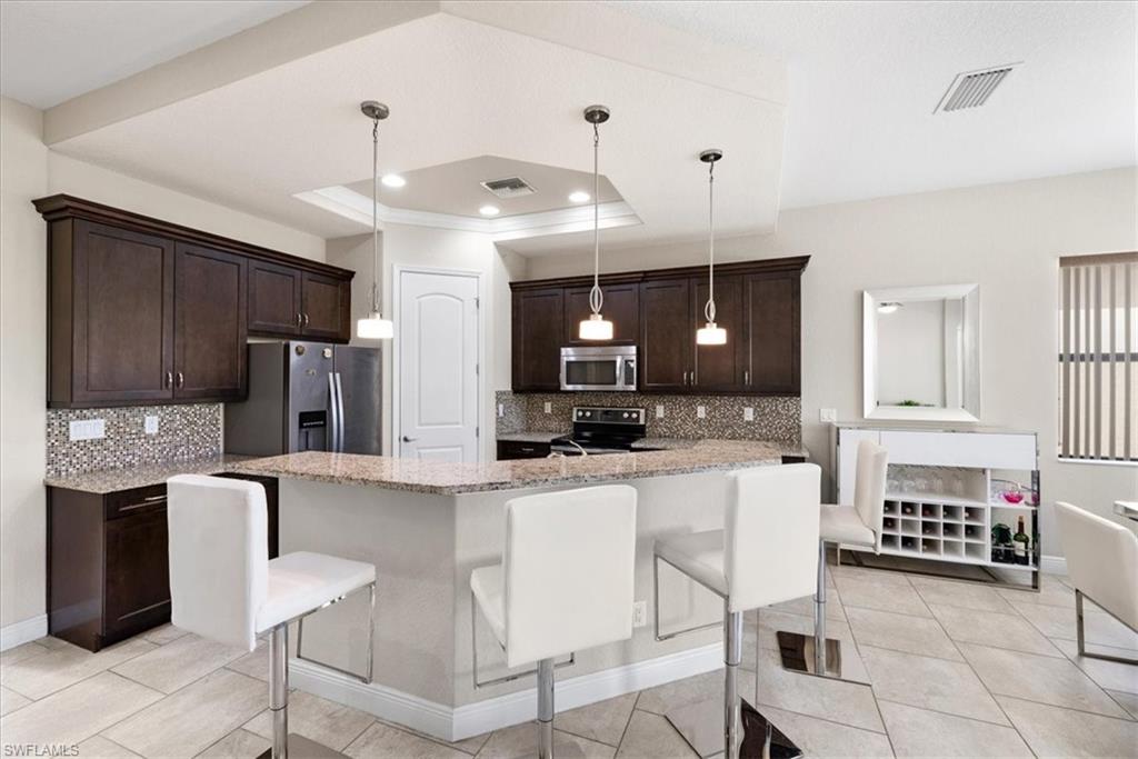 1509 Serrano Circle Naples, FL 34105 - Photo 5 of 24 a kitchen with stainless steel appliances kitchen island granite countertop a refrigerator a stove a sink a dining table and chairs with wooden floor