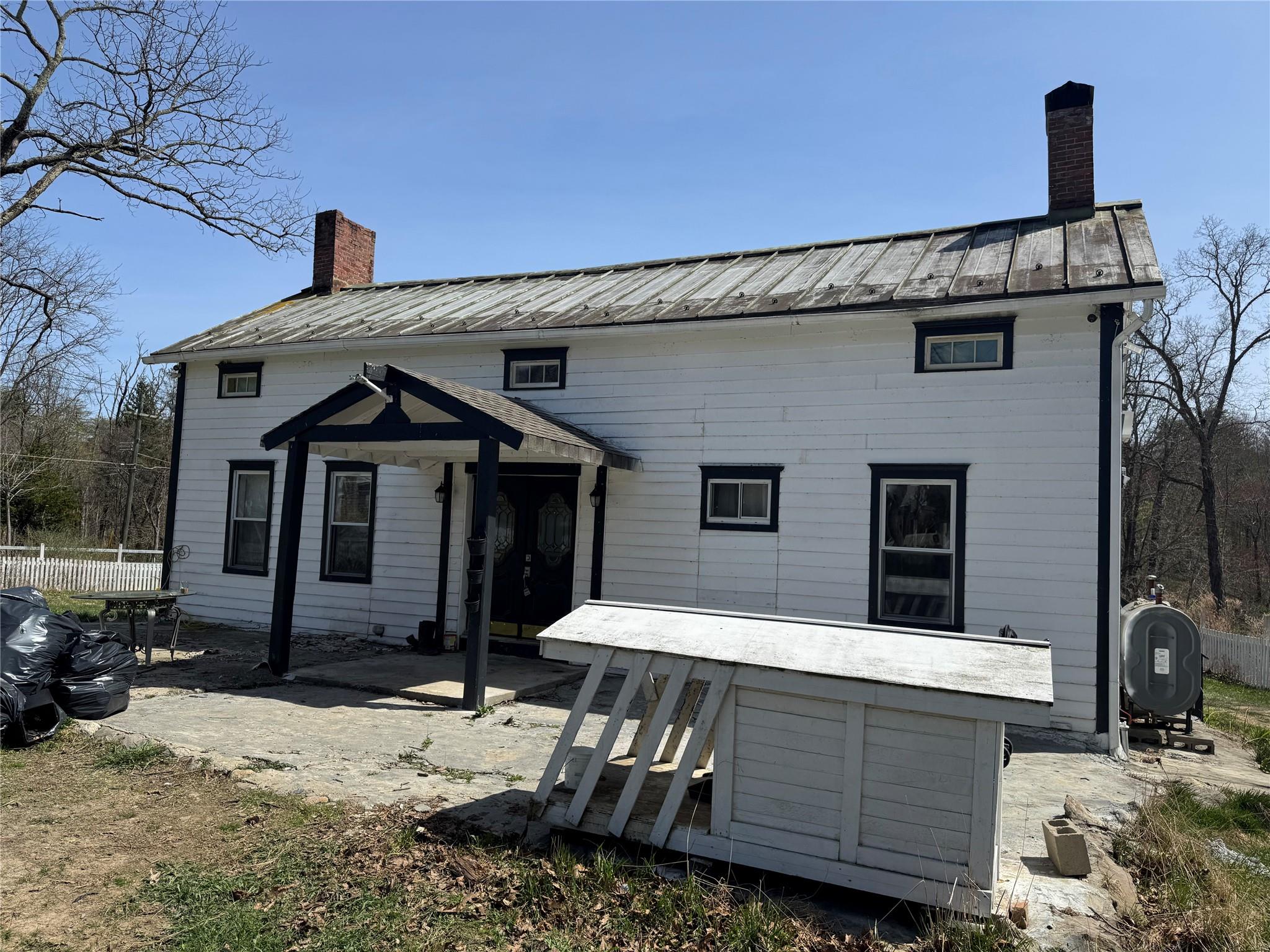 Back of house featuring a chimney, fence, heating fuel, and metal roof