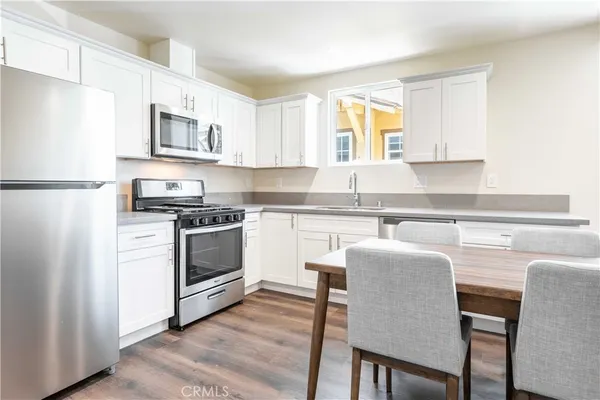 a kitchen with stainless steel appliances a stove a sink refrigerator and white cabinets with wooden floor