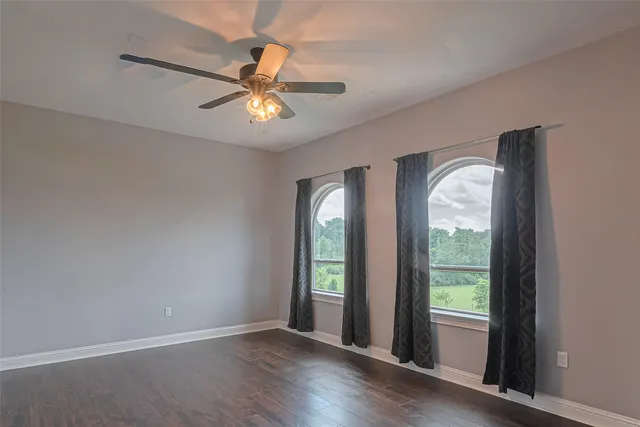 an empty room with wooden floor fan and windows