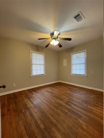 an empty room with wooden floor chandelier fan and windows