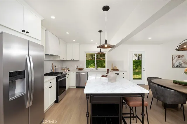 a kitchen with stainless steel appliances granite countertop a sink a stove a refrigerator cabinets and chairs