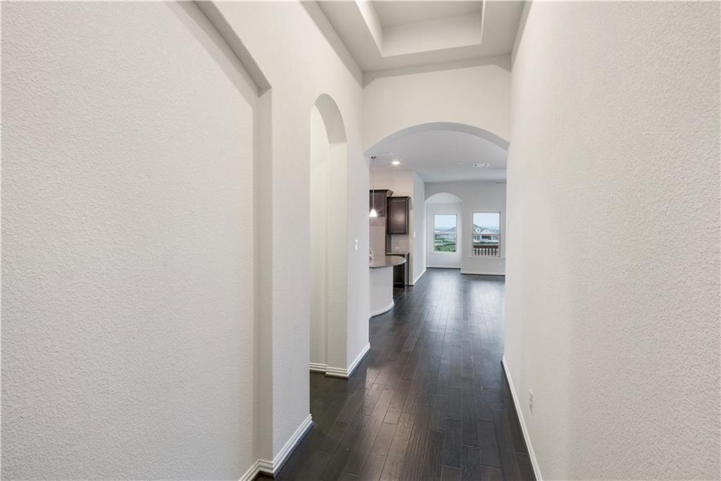 6752 Catania Loop Round Rock, TX 78665 - Photo 8 of 25 Hall featuring a textured wall, dark wood-style flooring, arched walkways, and a tray ceiling