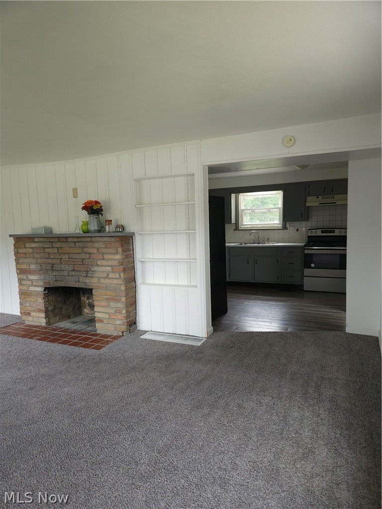 4660 Darrow Road Stow, OH 44224 - Photo 5 of 25 Open-concept living area featuring a brick fireplace with working hearth, neutral carpet flooring, white shiplap accent wall, and seamless access to a modern kitchen with dark cabinetry and stainless steel appliances