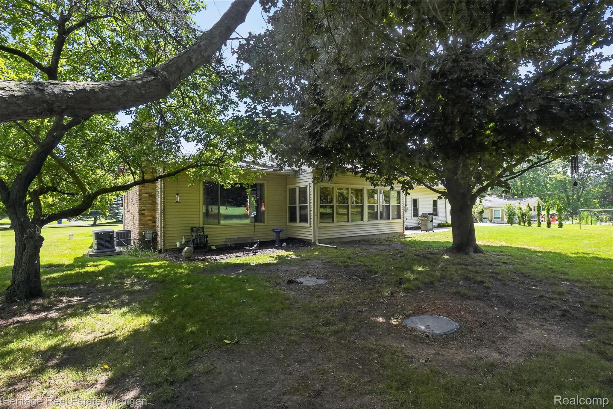 14038 North Hogan Road Linden, MI 48451 - Photo 41 of 53 Expansive rear yard featuring mature trees, a sunroom with multiple windows, and a yellow-toned siding exterior