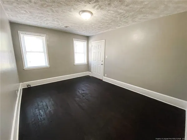 an empty room with wooden floor and windows with curtains