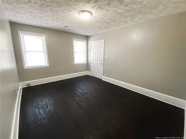 an empty room with wooden floor and windows with curtains