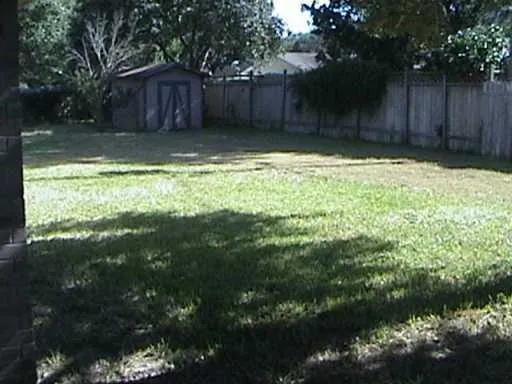 a view of a backyard with large trees and wooden fence