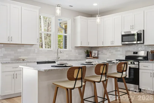 a kitchen with stainless steel appliances granite countertop a stove a sink dishwasher and white cabinets with wooden floor