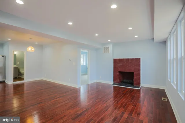 a view of an empty room with wooden floor fireplace and a window