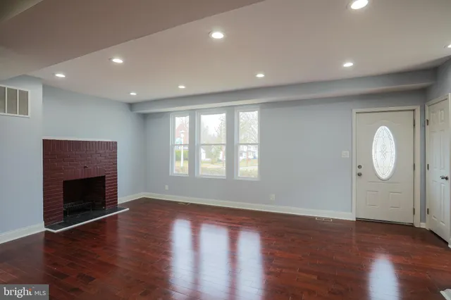 an empty room with wooden floor fireplace and windows
