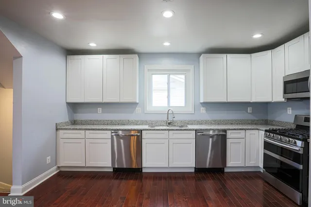 a kitchen with wooden floors white cabinets appliances and sink