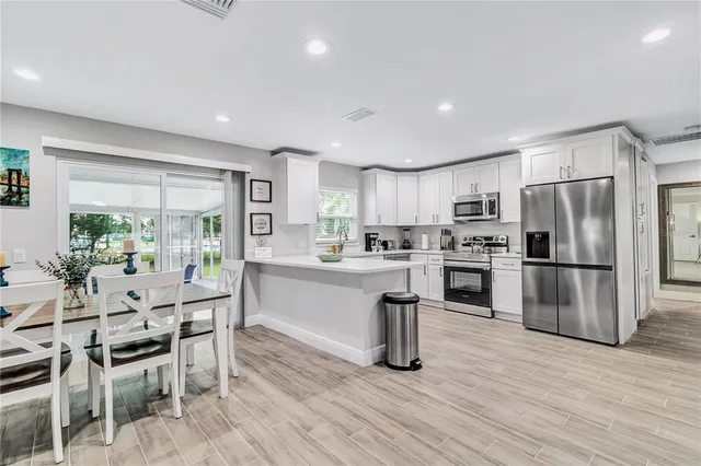 a kitchen with stainless steel appliances a refrigerator a stove top oven a sink dishwasher a dining table and chairs with wooden floor