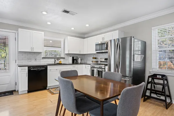 a kitchen with stainless steel appliances granite countertop a refrigerator a stove a sink a dining table and chairs with wooden floor