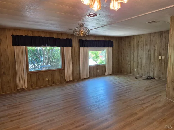 an empty room with wooden floor fan and windows