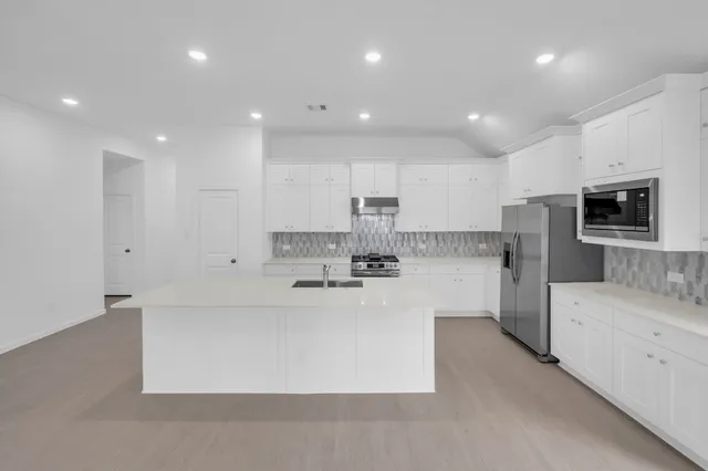 a large kitchen with kitchen island a sink a stove a refrigerator and white cabinets