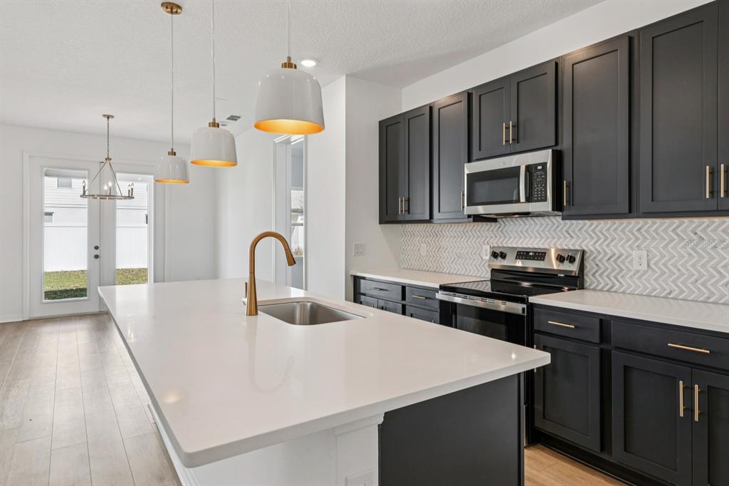 5721 Haystack Drive St. Cloud, FL 34771 - Photo 12 of 36 a kitchen with stainless steel appliances a stove a sink a microwave a refrigerator white cabinets and wooden floor