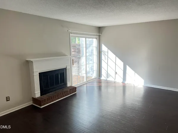 a view of an empty room with wooden floor and a fireplace