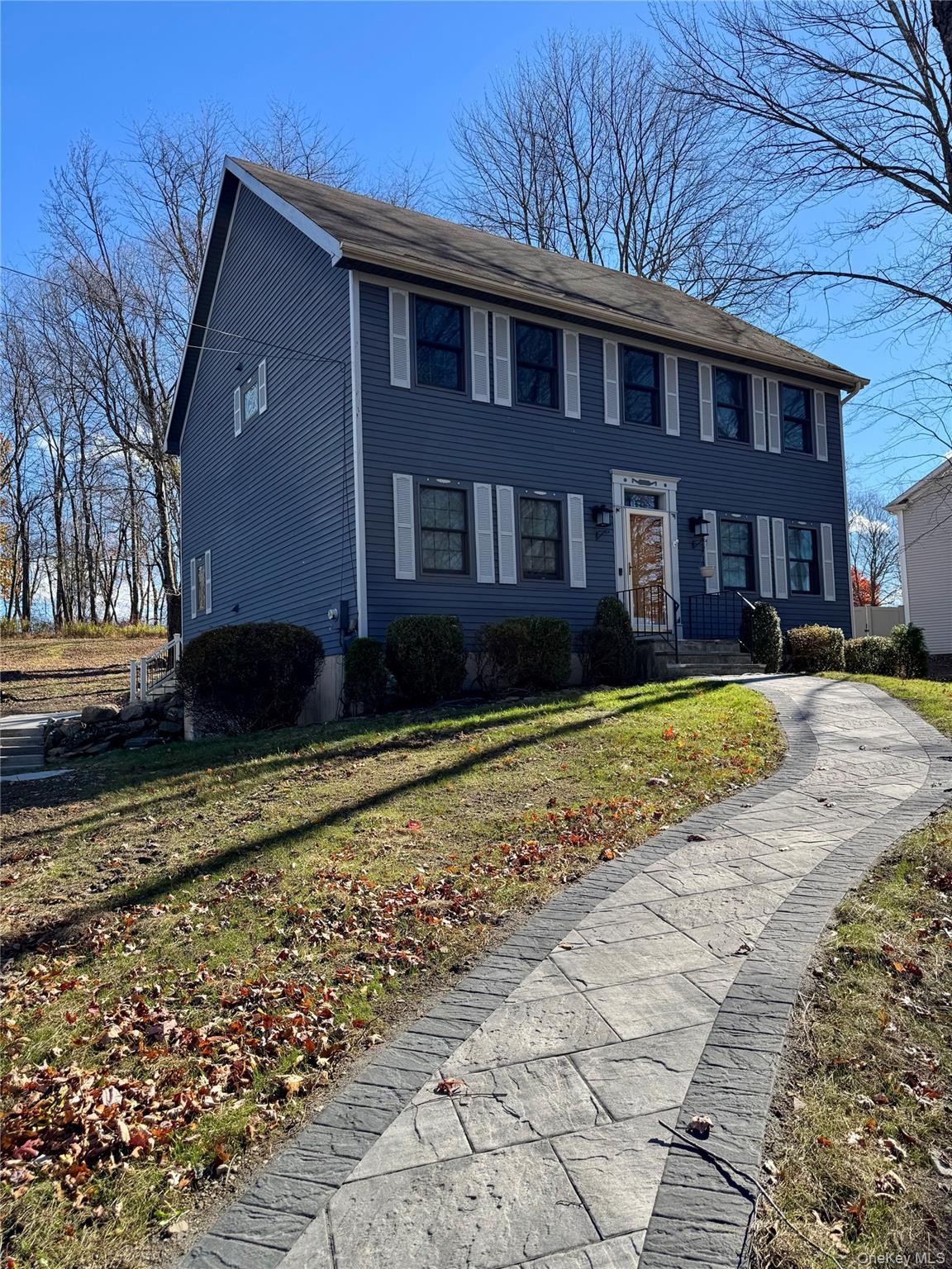 31 Denman Road Middletown, NY 10940 - Photo 2 of 18 The property features a two-story exterior with blue siding and white window shutters, complemented by a winding stone-patterned walkway leading to the entrance