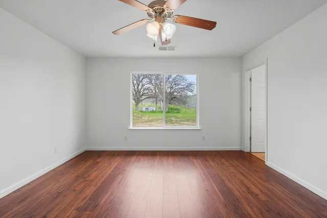 an empty room with wooden floor chandelier fan and windows