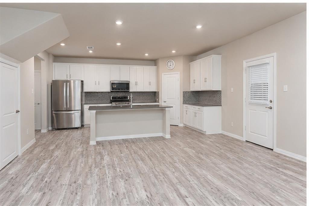 3704 Banton Street Rowlett, TX 75089 - Photo 5 of 16 Open-concept kitchen featuring white cabinetry, stainless steel appliances, a central island with a sink, grey stone countertops, and recessed lighting