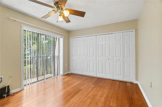 an empty room with wooden floor chandelier fan and windows