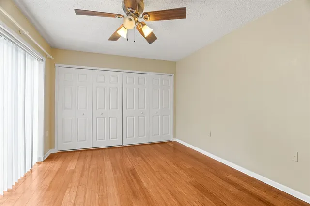 an empty room with wooden floor chandelier fan and windows