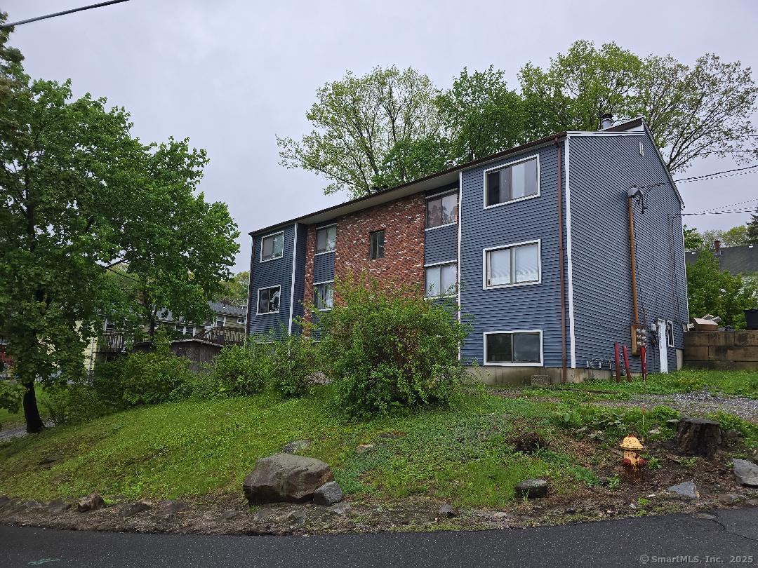 44 Armand Drive, Unit E Waterbury, CT 06708 - Photo 2 of 7 a brick house with a small yard and trees