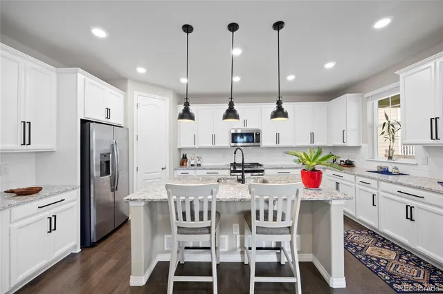 a kitchen with stainless steel appliances kitchen island granite countertop a table chairs stove and white cabinets