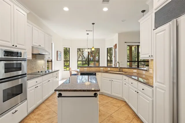 a large white kitchen with stainless steel appliances granite countertop a stove a sink and white cabinets