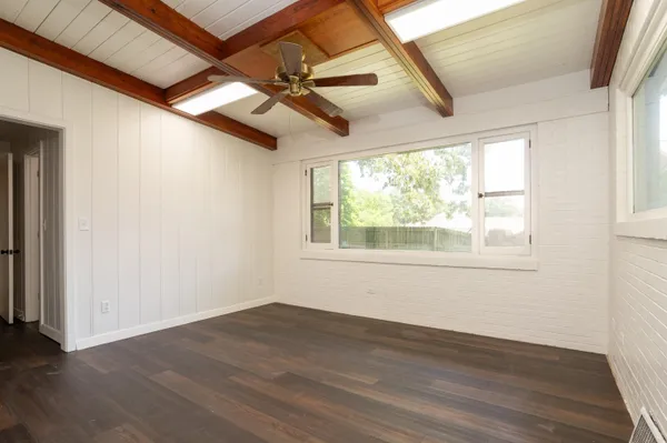 an empty room with wooden floor fan and windows