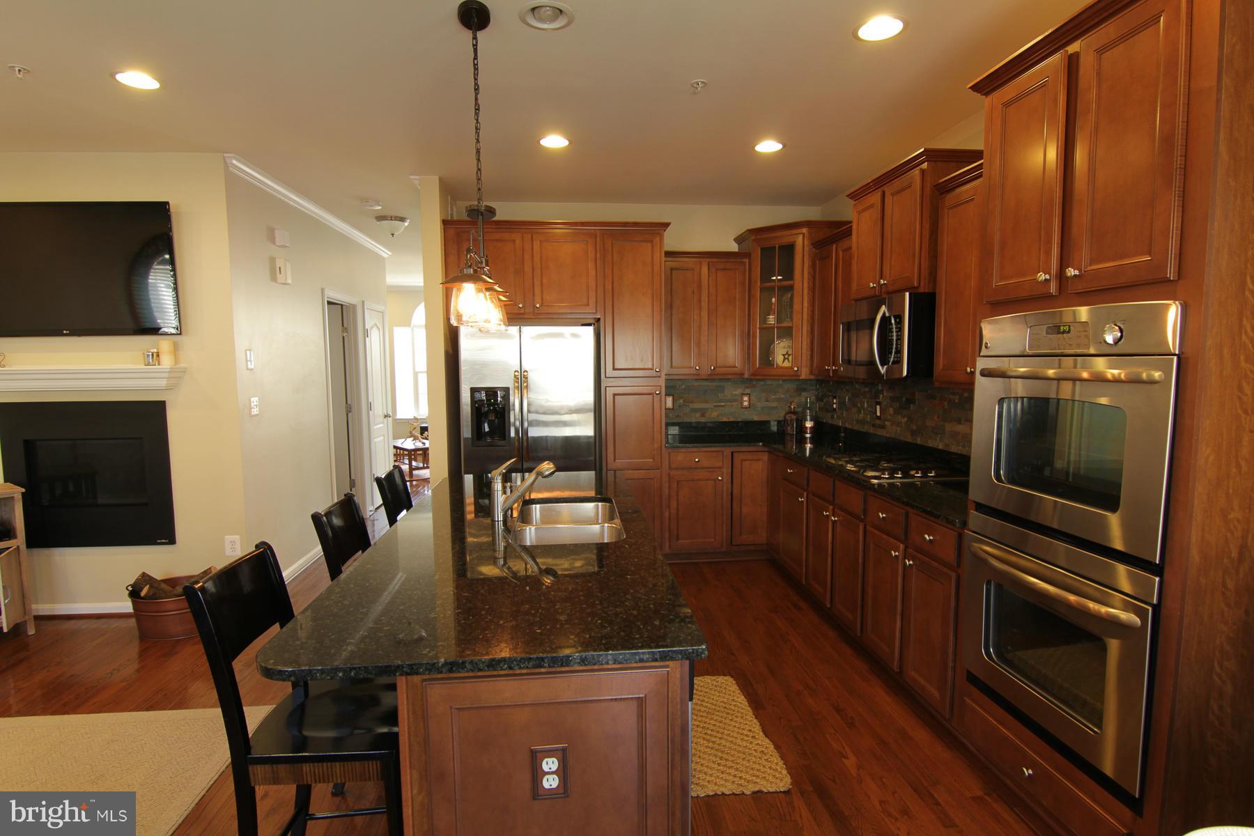 2651 Shade Branch Road Hanover, MD 21076 - Photo 25 of 30 a kitchen with stainless steel appliances kitchen island granite countertop a refrigerator a stove a sink a dining table and chairs with wooden floor