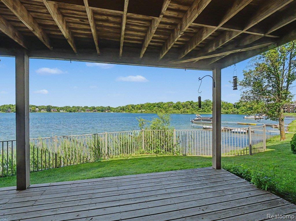 1974 Klingensmith Road, Unit 4 Bloomfield Hills, MI 48302 - Photo 25 of 35 Covered deck with wood plank flooring, overlooking a lake with docks, green lawn, and mature trees