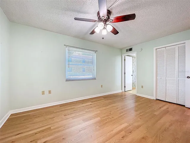 an empty room with wooden floor chandelier fan and windows