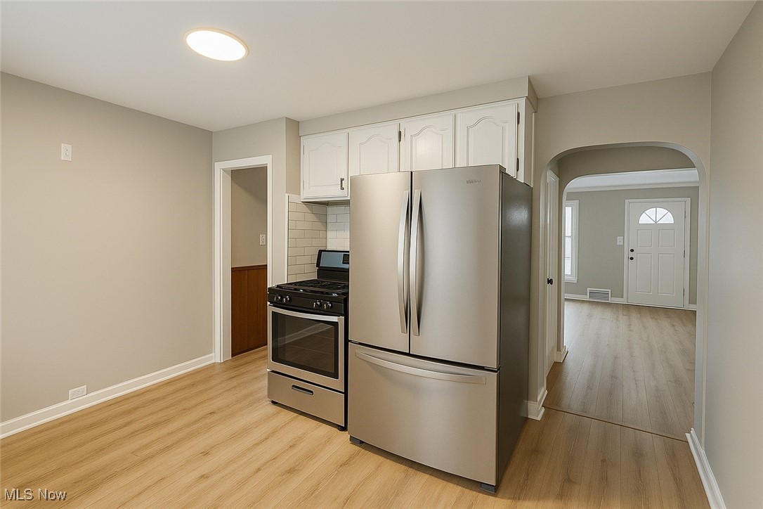 14505 Triskett Road Cleveland, OH 44111 - Photo 4 of 15 Kitchen with appliances with stainless steel finishes, white cabinetry, arched walkways, light wood-style flooring, and decorative backsplash