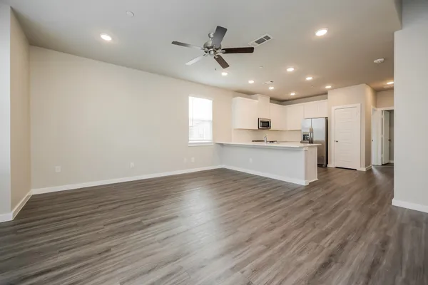 a view of an empty room with wooden floor and a kitchen