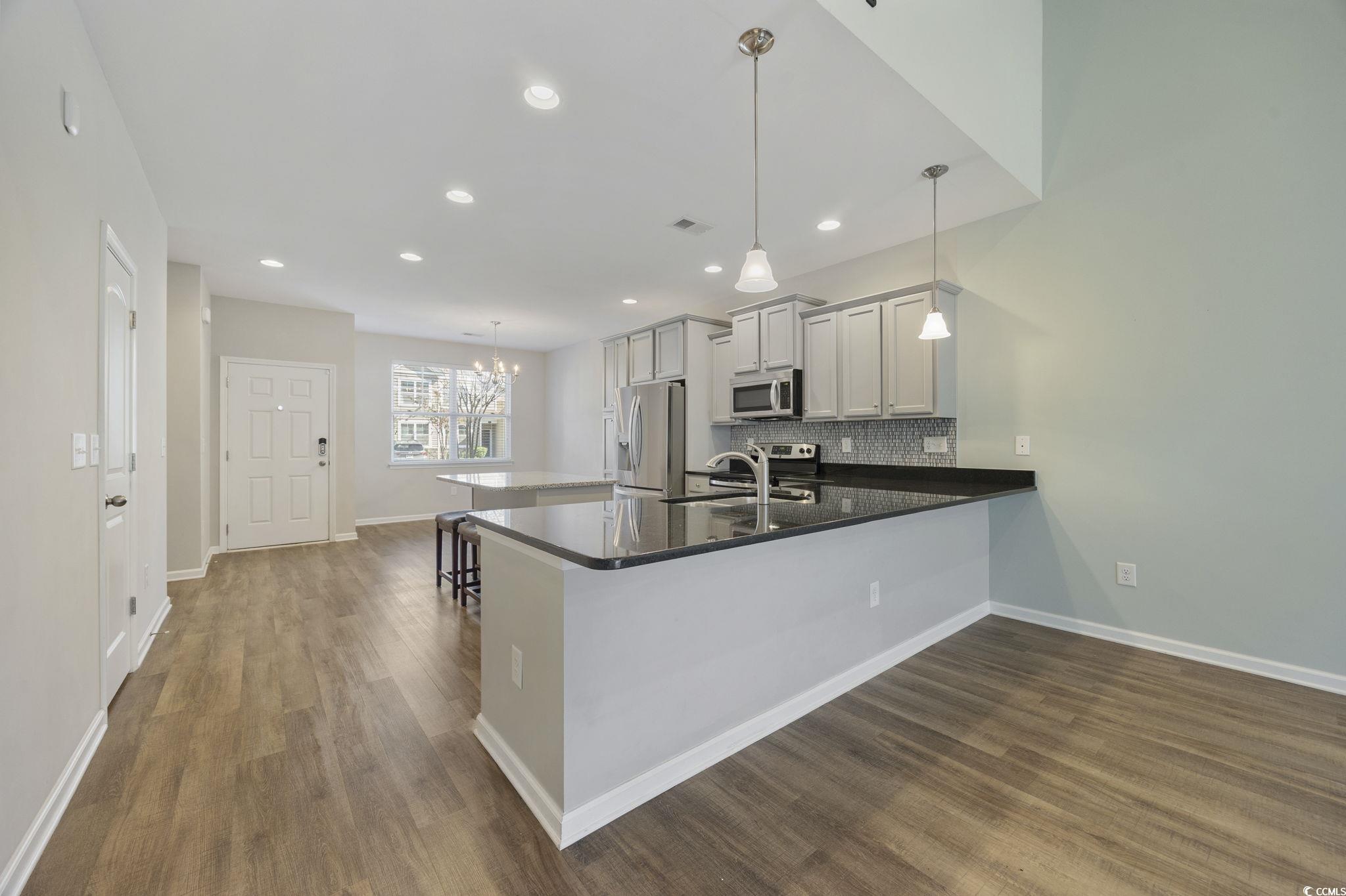 115 Machrie Loop, Unit D Myrtle Beach, SC 29588 - Photo 8 of 40 Kitchen featuring hanging light fixtures, tasteful backsplash, dark stone counters, a peninsula, and dark wood finished floors