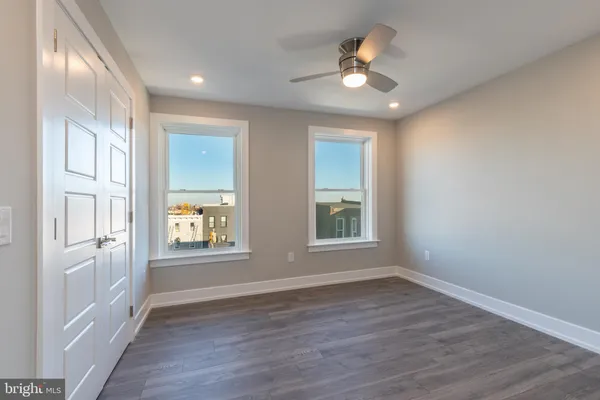 an empty room with wooden floor ceiling fan and windows