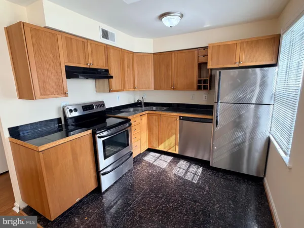 a kitchen with granite countertop a refrigerator a sink and wooden cabinets