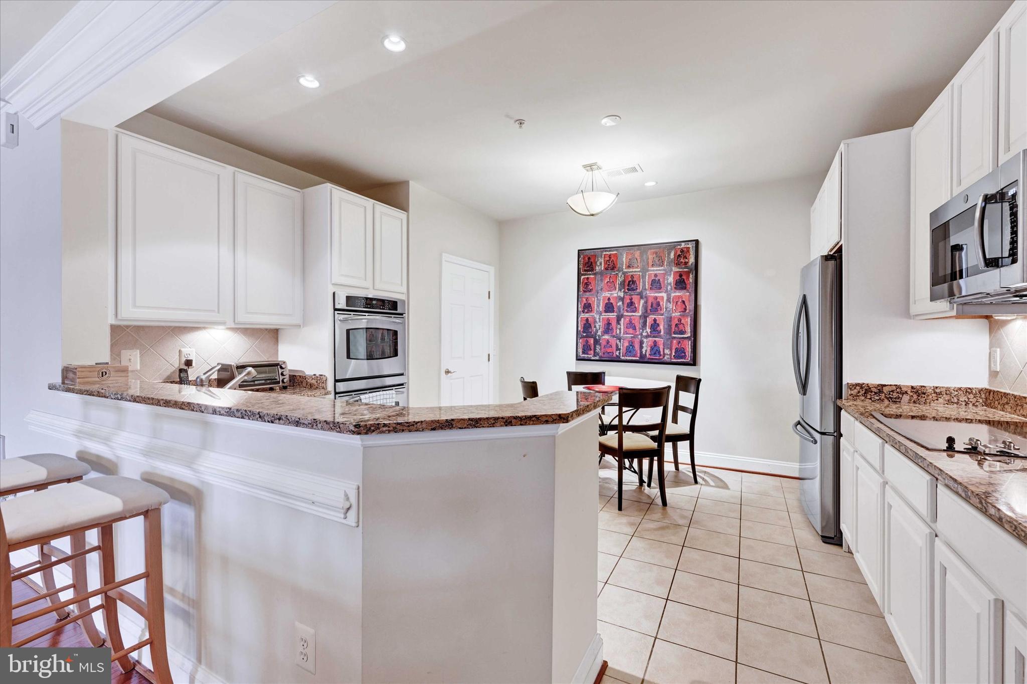 3000 Stone Cliff Drive, Unit 205 Baltimore, MD 21209 - Photo 11 of 28 a kitchen with stainless steel appliances granite countertop a stove top oven a sink a dining table and chairs with white cabinets