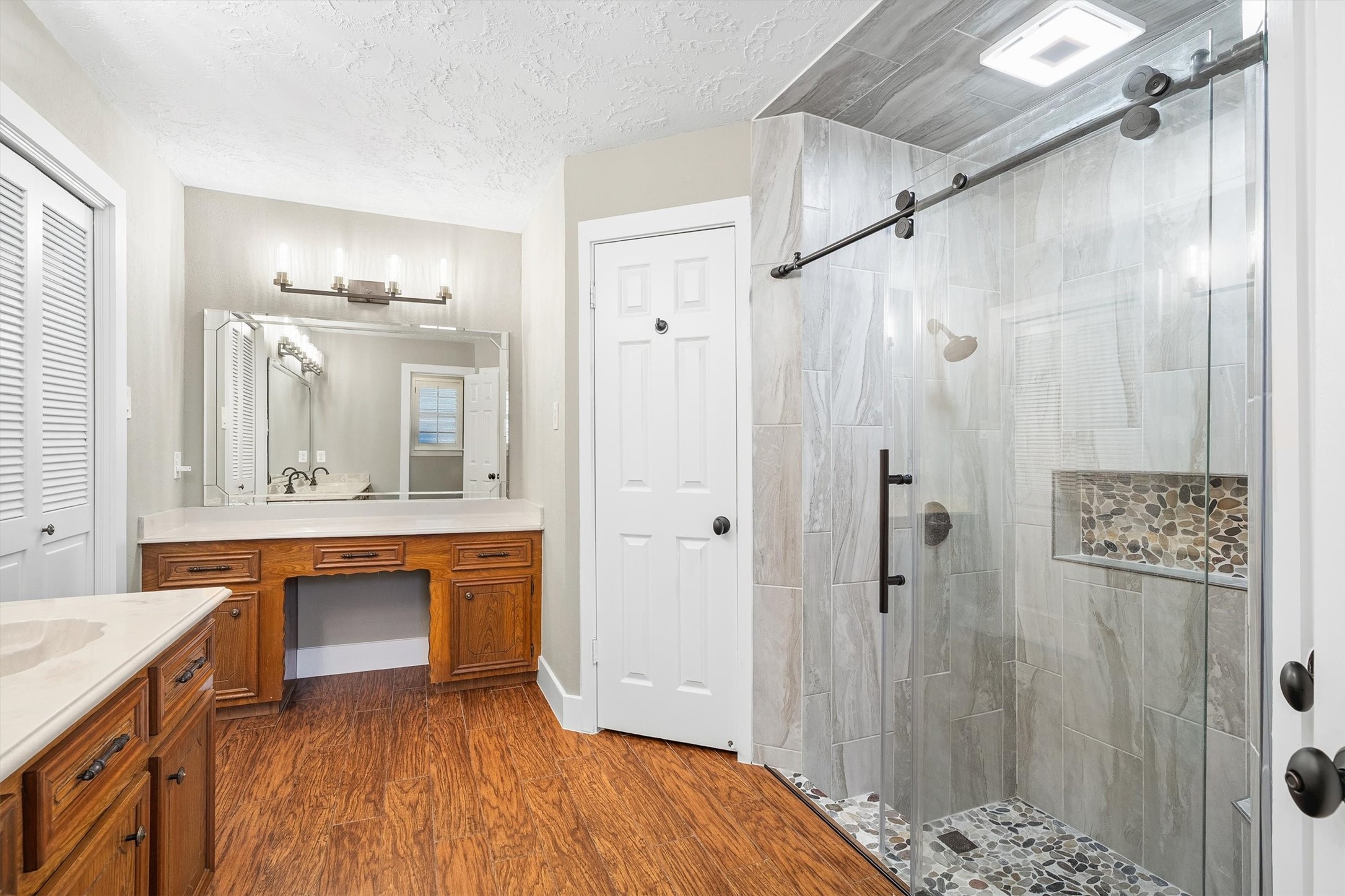 826 North Rivershire Drive Conroe, TX 77304 - Photo 23 of 46 From this angle the full primary bath layout comes together. Upgraded frameless glass shower, double vanity with cultured marble, built-in vanity desk, and wood look flooring throughout. This bathroom was thoughtfully redone and it shows