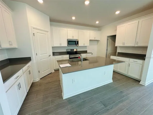 a kitchen with stainless steel appliances a stove top oven a sink a refrigerator white cabinets and wooden floor