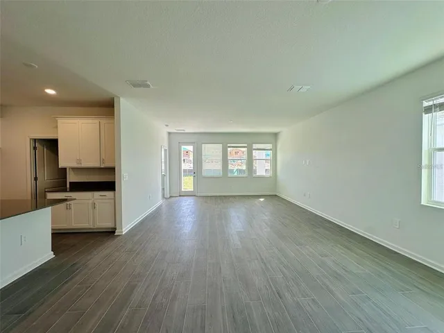 a view of a kitchen and an empty room with wooden floor and a window