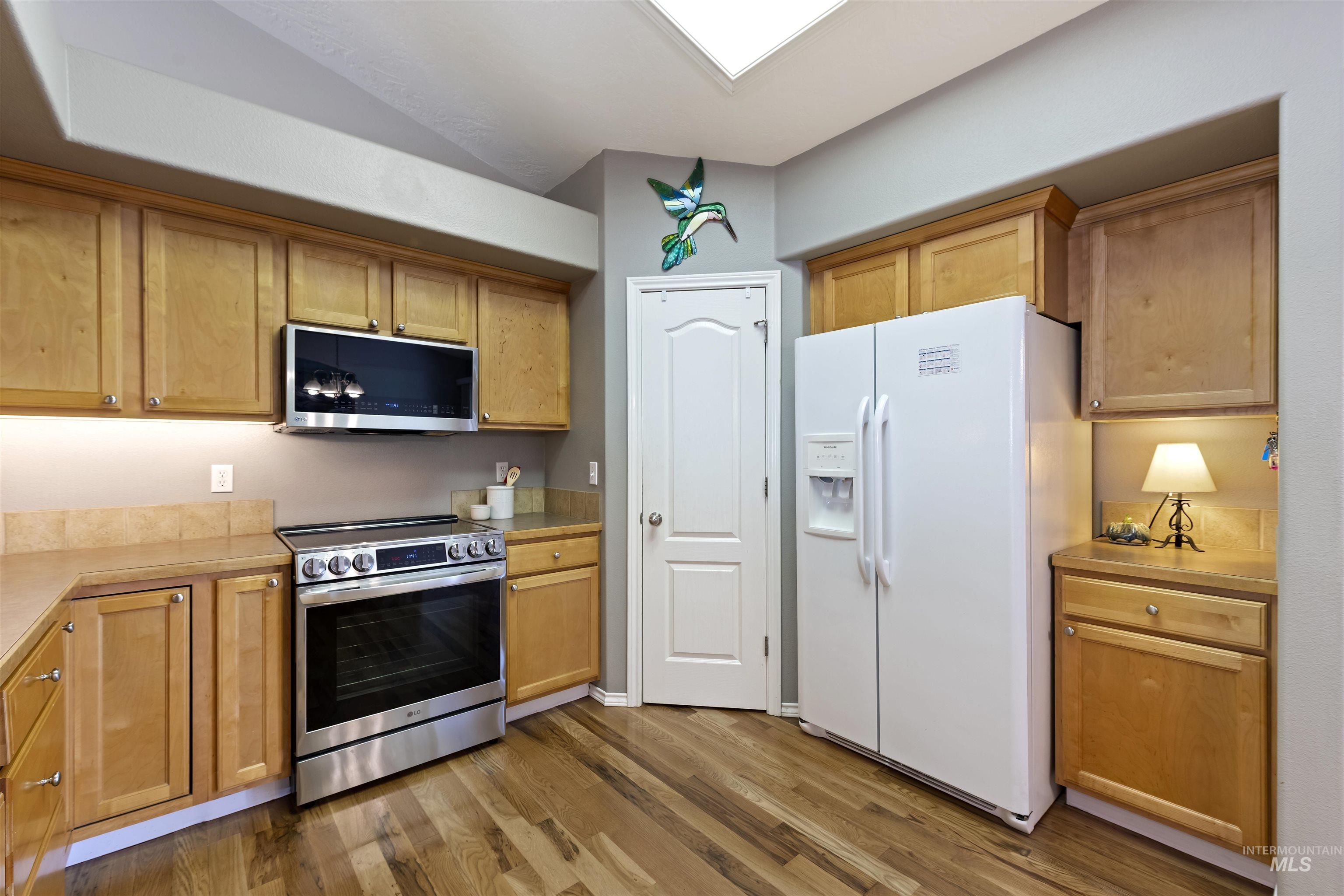 2175 North CapeCod Way Meridian, ID 83646 - Photo 11 of 23 Kitchen featuring wood-finish flooring, light wood cabinetry, stone-finish countertops, a tile backsplash, and a stainless steel range with an overhead microwave