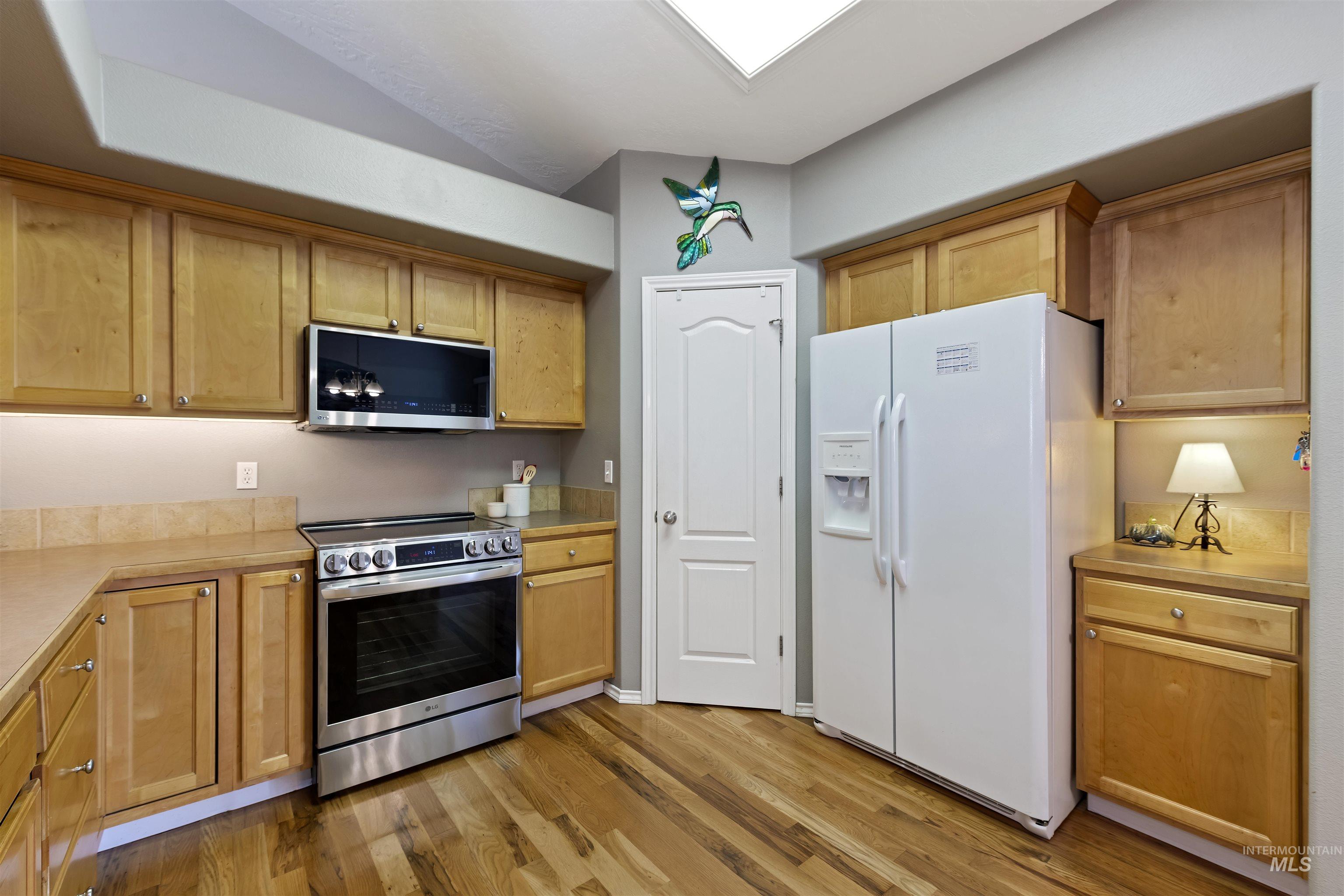 2175 North CapeCod Way Meridian, ID 83646 - Photo 12 of 23 Kitchen featuring wood-finish flooring, light wood cabinetry, neutral countertops, stainless steel range, and an overhead microwave