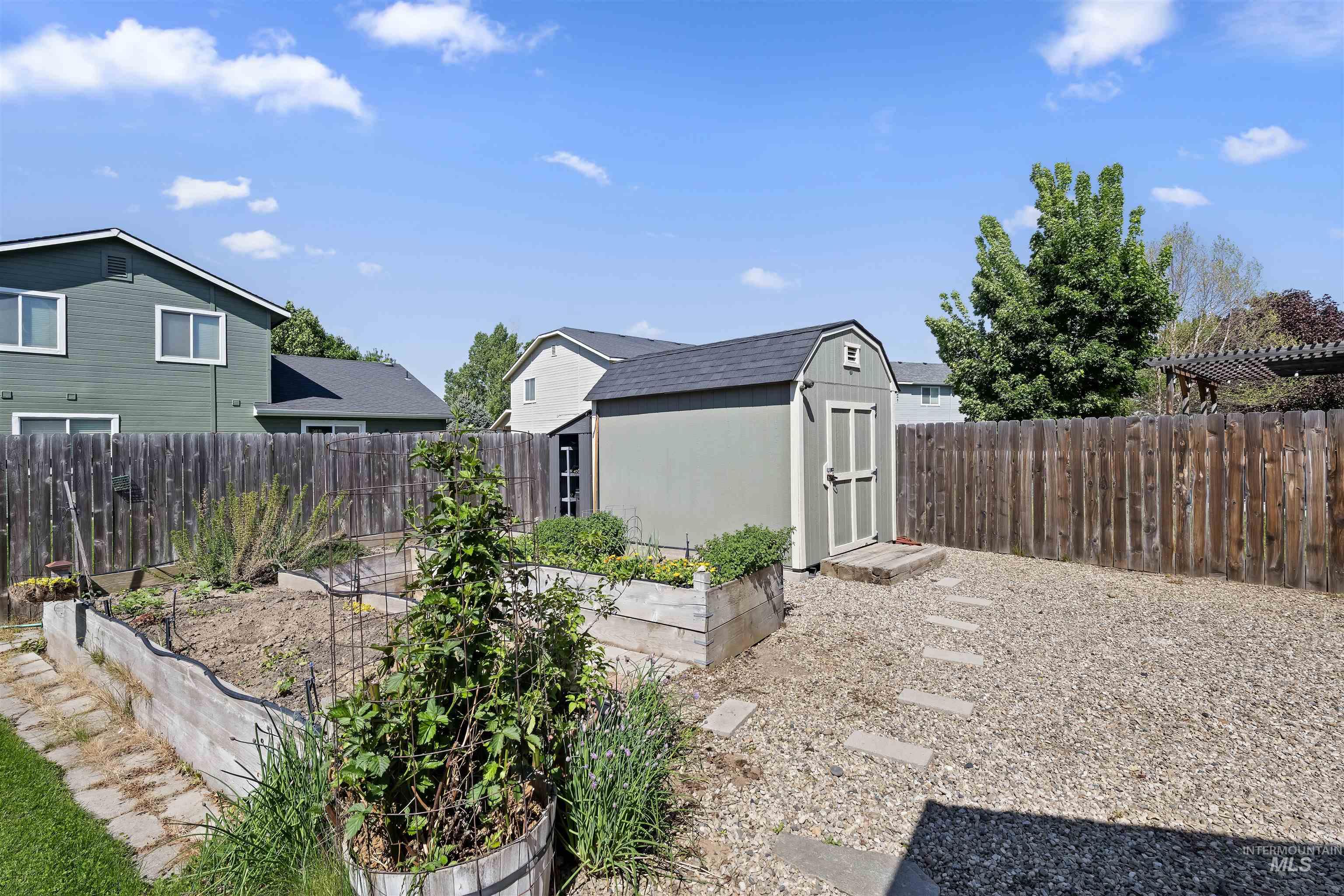 2175 North CapeCod Way Meridian, ID 83646 - Photo 22 of 23 Backyard featuring a gravel patio, raised garden beds, and a storage shed with an asphalt shingle roof