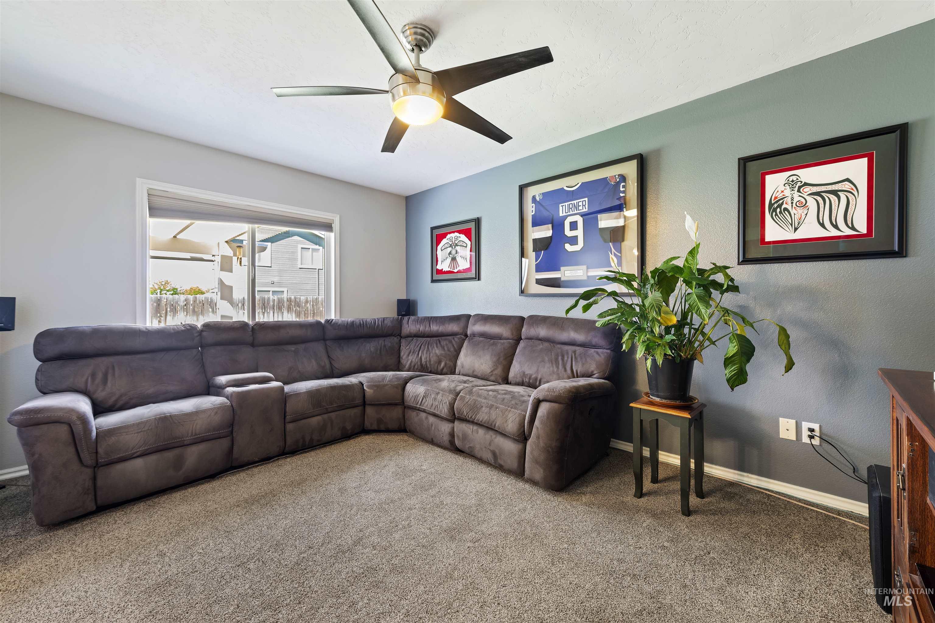 2175 North CapeCod Way Meridian, ID 83646 - Photo 6 of 23 Spacious living area featuring neutral-tone carpeting, a large window, a ceiling fan with integrated lighting, and a neutral wall color palette
